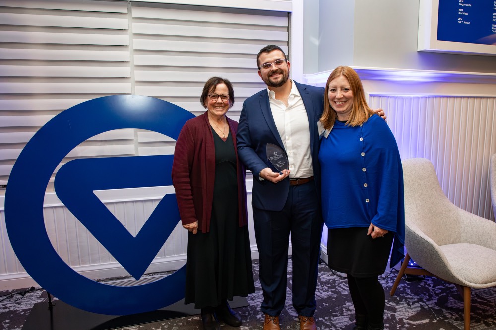 Alex Hogarth poses with two women in front of GVSU logo sign